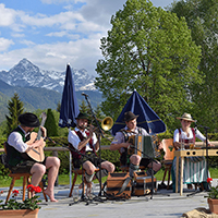 Sitzende Musiker mit u.a. Gitarre, Posaune, Akkordeon vor Bergkulisse