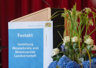 Blumenschmuck, Rednerpult, Plakat mit Text: Festakt, Verleihung Meisterbriefe und Meisterpreise Lanswirtschaft, Link öffnet Großansicht des Bildes